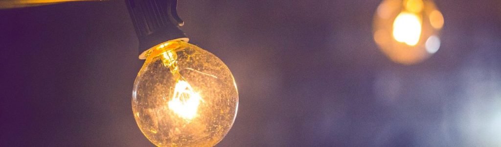 Close-up of an illuminated vintage-style string light bulb on a dark background.