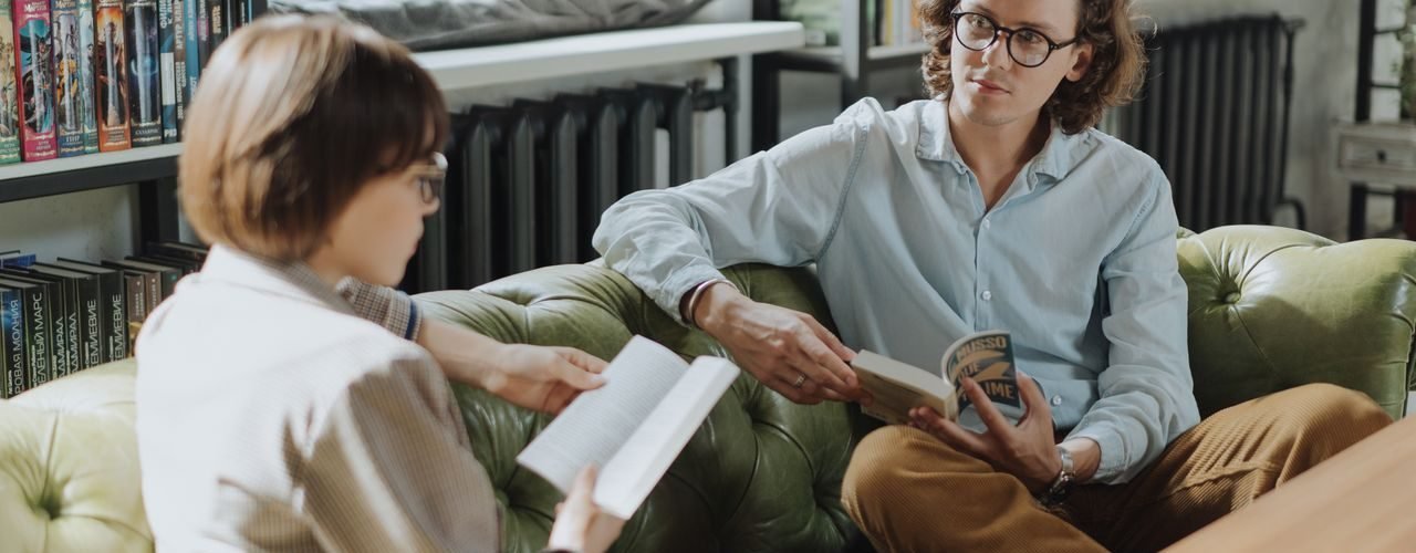 Two young adults enjoying a cozy moment reading and discussing books in a library.